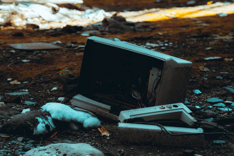 A large pile of discarded mobile phones and feature phones, with varying sizes, shapes, and colors, including black, white, silver, and red. The phones exhibit different textures, with some having glo