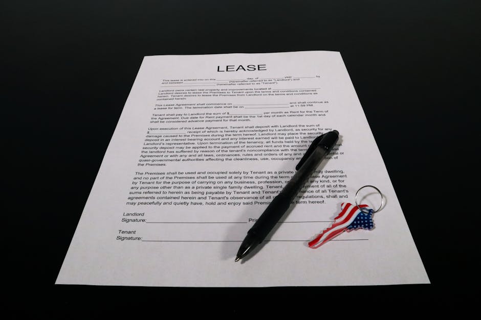 A printed lease agreement document laying flat on a dark, smooth surface, with visible black text outlining tenancy terms and signatures at the bottom. Resting diagonally across the paper is a black b